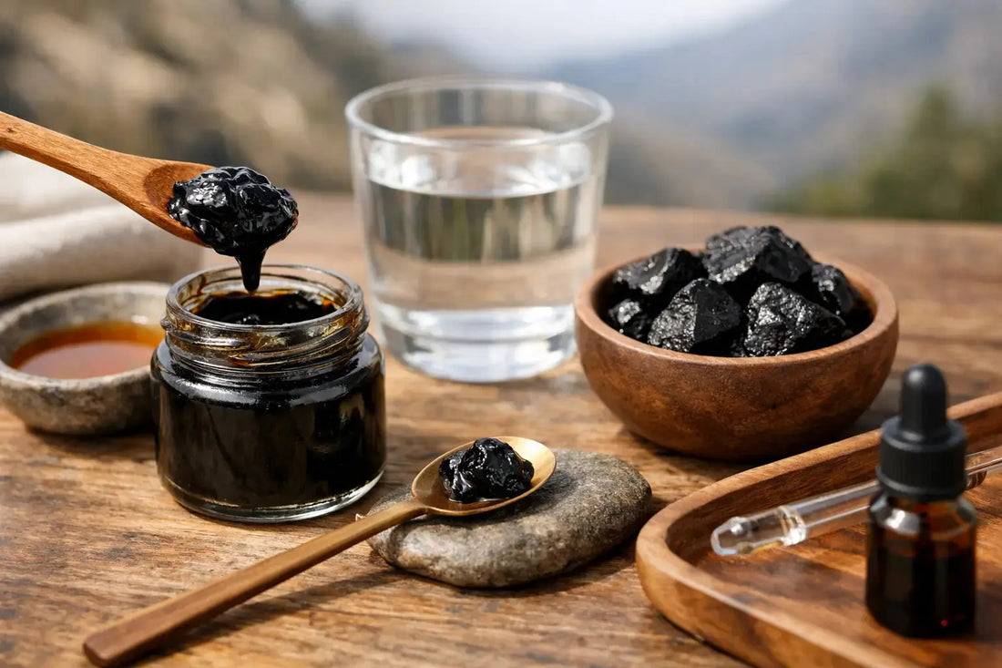 Resin shilajit in a jar with wooden spoon, chunks in a bowl, and a glass of water on a wooden table