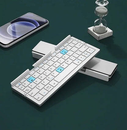 Compact white keyboard with bluetooth folding design placed near smartphone and hourglass