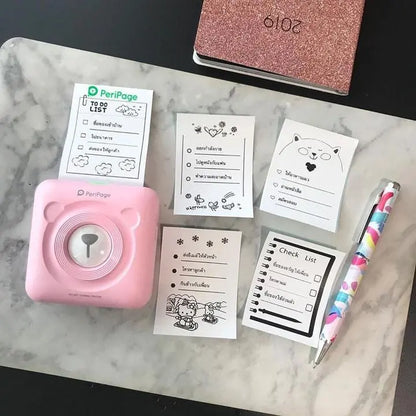 Pink PeriPage mini portable printer on marble table with printed to-do list notes and colorful pen